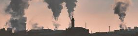 smoke is emitted from buildings with pink sunset behind